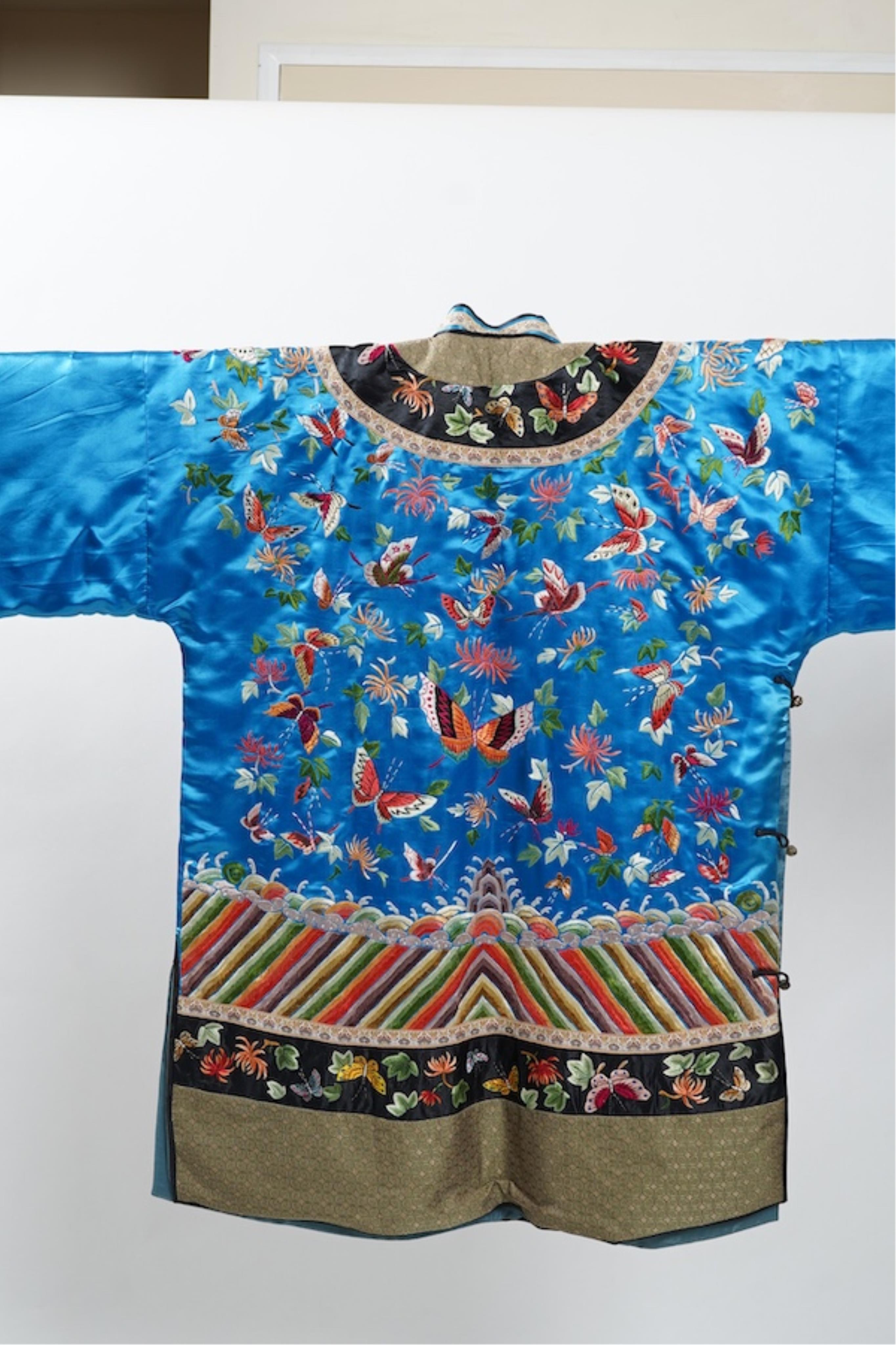 A mid 20th century Chinese turquoise silk jacket, with all over polychrome butterfly embroidery, similar embroidered sleeve bands, front and bottom edges on black silk, all bordered with gold brocade. The jacket blue sil
